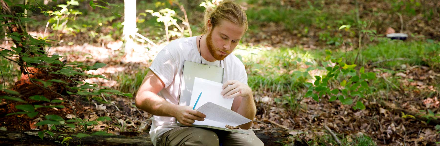 A young man wearing work clothes conducts field research in a forest.